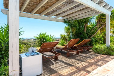 Bahçede çam ormanı manzaralı bir çardak turistlerin dinlenebileceği bir yer. Dinlenmek için güneş yatakları, içmek için tepside bardaklar..