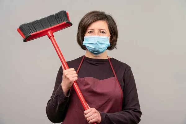 Μια γυναίκα με χειρουργική μάσκα, μια μεσήλικη Ευρωπαία, μια καθαρίστρια, κρατάει μια σφουγγαρίστρα στα χέρια της. Η έννοια του καθαρισμού . — Φωτογραφία Αρχείου