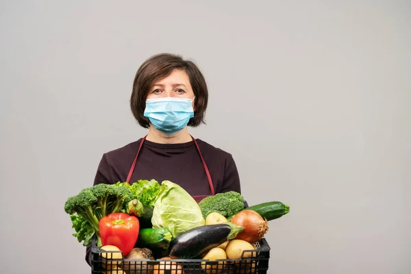 Una donna in maschera chirurgica, un europeo di mezza età, un volontario, consegna cibo e verdura a chi ne ha bisogno durante la pandemia.. Foto Stock