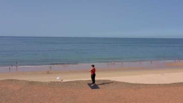 Eine Frau mittleren Alters blickt nach Sport, Aufwärmen und Gymnastik in einem ruhigen Zustand auf das Meer. Direkt am Meer mit Blick auf den Strand. Sonniger Tag. — Stockvideo