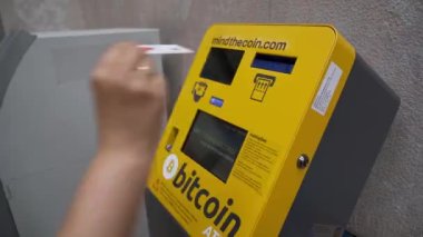 Orta yaşlı bir kadın bitcoin ve altsikke almak ve takas etmek için ATM 'ye kredi kartıyla giriyor. Yakın plan..