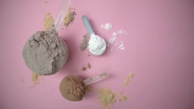 El, bir ölçüm kabını pembe arka planda protein tozuyla birlikte farklı spor takviyeleri içeren bir grup diğer ölçüm kabına yerleştirir..