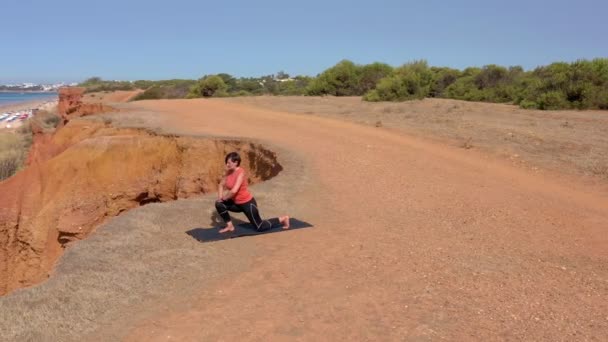 En medelålders kvinna på havets strand går in för sport, gymnastik. Träna lungor. På stranden med utsikt över stranden. Seascape i bakgrunden. — Stockvideo