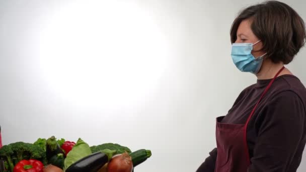 Een vrijwilliger distributeur, die een doos overhandigt aan een gemaskerde vrouw met verse groenten voor mensen in nood. In tijden van crisis of pandemie, de armen. — Stockvideo