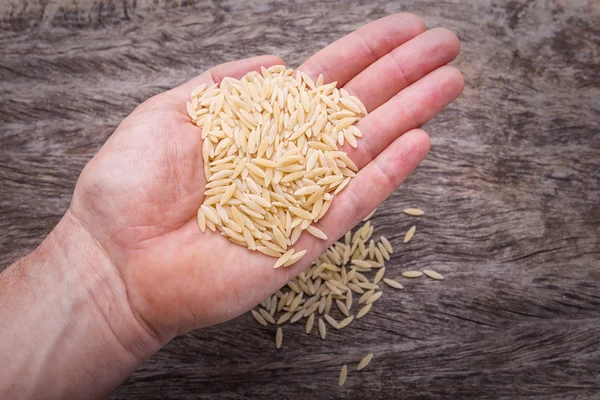 Arroz cru na mão de um homem. Sobre um fundo de uma textura de madeira. — Fotografia de Stock