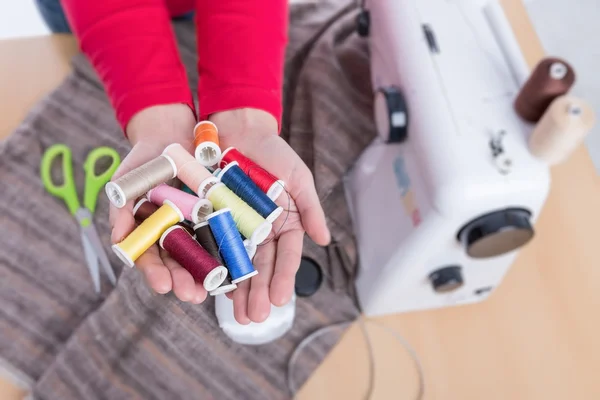 Naaigarens in de handen van een naaister. Naaimachine op de achtergrond. — Stockfoto