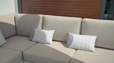 Sıcak güneş ışığı çağdaş açık hava kanepesinde parıldıyor, zarif bej yastıkları ve çizgili aksan yastıkları birden fazla tasarım perspektifinden vurguluyor.