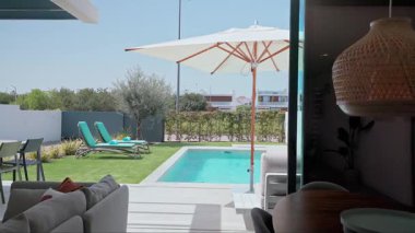 Modern villa, özel bir yüzme havuzu, güneş pansiyonları, yapay çimleri olan bir bahçe ve kısmen görünür bir iç mekan.