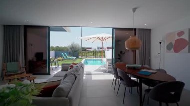 Çağdaş villa, kapalı ve açık havada yaşam arasında pürüzsüz bir geçiş sergiliyor, şık bir oturma odası ve yemyeşil bir havuzu var.