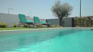 Turkuaz su, el değmemiş beyaz güverte ve yapay çim ile çevrili modern bir yüzme havuzunda parıldıyor. İki boş iskemle konukları dinlenmeye ve güneşli günün tadını çıkarmaya davet ediyor.