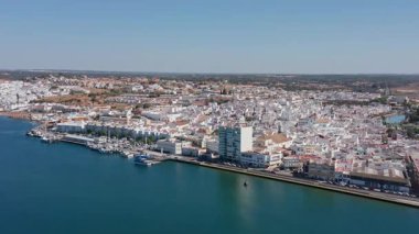 Ayamonte 'nin insansız hava aracı görüntüsü beyaz binalar, rıhtım ve demirlemiş tekneler, rıhtım kafeleri ve teraslar üzerindeki sıcak ışıkla birlikte havadan görüntüsü Guadiana' ya yansıyor.