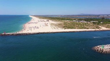 Tavira Portekiz 'in insansız hava aracı görüntüsü. Güneşli plaj şemsiyeli ve turkuaz deniz manzaralı. Tavira kumlu cankurtaran gözlemi ve dalgaların keyfini çıkaran aileler, plaj şemsiyeleri.,
