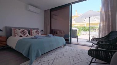 Modern otel odası doğal ışıkla yıkanmış, içinde deniz mavisi yatak örtüsü, pembe yastıklar, komodinlerin yanında masalar, klima ve rahat bir atmosfer yaratan özel bir teras var.