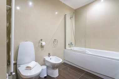 Temiz ve modern bir banyoda banyo, duş ve tuvalet sergileniyor. Tarafsız fayanslar ve modern aksesuarlarla vurgulanarak rahatlatıcı bir alan yaratılıyor..
