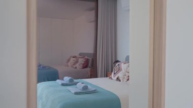 Yumuşak, düzgünce katlanmış açık mavi havlular turkuaz yatak örtüsünün üzerinde dinleniyor. Kısmen açık otel odasının kapısından davetkar bir atmosfer yaratıyor.