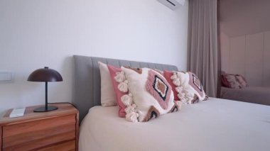 Teal battaniyesi ve dekoratif yastıklar modern ve minimalist bir yatak odasında bir yatak süslerken, katlanmış mavi havlular misafirler için hazırlanmayı öneriyor.