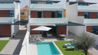 Şatafatlı beyaz şemsiye, modern villanın yanındaki el değmemiş yüzme havuzunun üzerine yavaş yavaş açılıyor. Akdeniz mimarisinin zarafetini ve yaz rahatlığını simgeliyor.