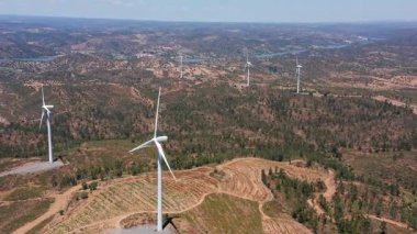 Kırsal alanlara entegre rüzgar türbinleri yumuşak teraslar, dolambaçlı yollar ve dağınık kuleler gösteriyor yenilenebilir altyapıyı tarımsal yamaçlara getiriyor.