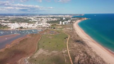 Alvor hava manzaralı insansız hava aracı kıyı şeridi altın plaj ve turkuaz deniz, kum tepecikleri ve tatil köyünün ufuk çizgisine uzanan yakındaki golf sahaları, kumlu kıyıların kenarındaki berrak mavi su, ideal.