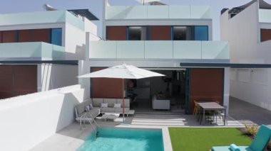 Modern lüks bir villanın bahçesinde yüzme havuzu ve açık hava mobilyası olan büyük beyaz veranda şemsiyesi, rahatlatıcı ve rahat bir açık hava alanı yaratıyor.