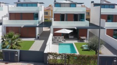 Özdeş beyaz ve kahverengi villalarda özel havuzlar, yapay çim çimenleri ve açık hava mobilyaları, çağdaş bir konut kompleksinde rahat ve şık bir yaşam sunuyor.