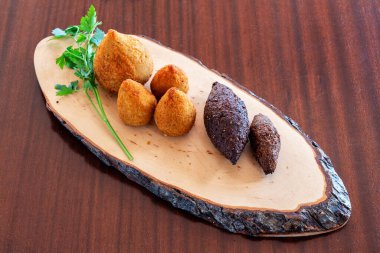 Çeşitli hindiba ve kibe taze otlarla süslenmiş ahşap bir tabakta sunuluyor. Brezilya mutfağının canlı dokularını ve renklerini vurguluyorlar.