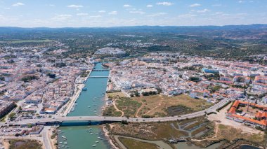 İnsansız hava aracı Tavira 'yı binaları, Gilao nehri ve küçük tekneleriyle yakalar. Panorama manzarası manzarayı ve Portekiz 'deki Algarve bölgesine olan bağlantıyı gösterir.
