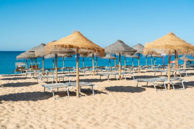 Saman şemsiyeler kumsalda gölge sağlar, dinlenme yerlerinin sakin suyun yanında, açık bir gökyüzünün altında oturduğu yerde..