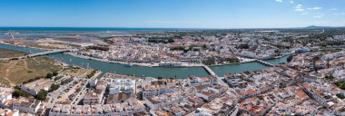 Algarve 'de Tavira, açık gökyüzü ile nehir ve beyaz binaların yer aldığı bir tepeden görülmektedir. Manzara, kasabaların yerleşim yerlerini ve çevresindeki manzarayı yakalar. Panorama Nehri Gilao ve Roma köprüsü