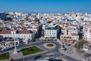 Ziyaretçiler rıhtım yakınlarındaki Faros Eski Kasabası sokaklarında yürürken, Algarve 'deki açık mavi gökyüzü altındaki mimari ve yerel dükkanların keyfini çıkarıyorlar..