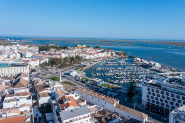 Ziyaretçiler, teknelerin demirlediği Faro, Algarve 'deki canlı rıhtımın keyfini çıkarıyorlar. Eski kasaba Ria Formosa ve çevresindeki binaların manzarasını sunuyor..