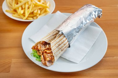 Lezzetli tavuk kebabı, altın kızartmaların yanında beyaz bir tabakta sunuluyor, taze malzemelerin altını çiziyor ve sıradan bir yemek düzeninde dokuları davet ediyor.