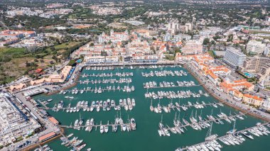 İnsanlar, Portekiz 'in Algarve kentindeki Vilamoura marinasında tekne, dükkan ve restoranlarla çevrili günün tadını çıkarıyorlar. Ziyaretçiler rahatlayıp bu canlı bölgeyi keşfediyorlar. Havadan