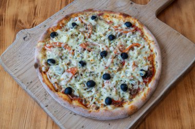 Lezzetli zeytinli ve erimiş peynirli pizza, sade ahşap bir tahtada sunuluyor, iştah açıcı dokuları ve davetkar görünümü vurguluyor.