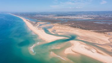 Bu hava görüntüsü Portekiz 'de Ria Formosa ve Praia de Faro' yu, açık gökyüzünün altında kıyı şeridini, su yollarını ve kumlu sahili göstermektedir..