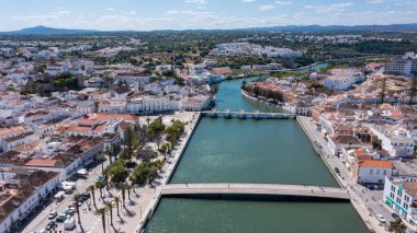 Bu hava manzarası Tavira 'yı Algarve' de, yeşil tepeler ve parlak gökyüzü ile çevrili nehir, Roma köprüsü ve beyaz binalarıyla yakalar..