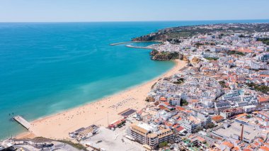 İnsanlar Albufeira 'daki plajda boş zaman aktivitelerine katılıyorlar. Marina ve kasaba turistler için güneşli günün tadını çıkaracak bir zemin hazırlıyor..