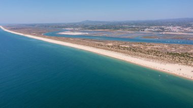 Tavira Portekiz Algarve. Berrak turkuaz suları ve yumuşak kumlu kıyıları olan sakin sahil perspektifi, doğal güzelliği ve sahil şeridinin barışçıl atmosferini vurguluyor.