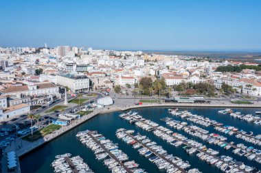 Ziyaretçiler Faro, Algarve 'deki marina manzarasının keyfini çıkarırken, tekneler kenetlendi ve eski kasaba açık gökyüzünün altında görülüyor. Bu bölge yıl boyunca birçok turisti cezbediyor..