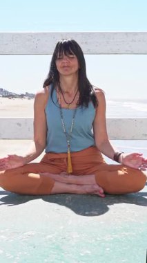 Dua eden bir kadın okyanus manzaralı bir rıhtımda poz veriyor.