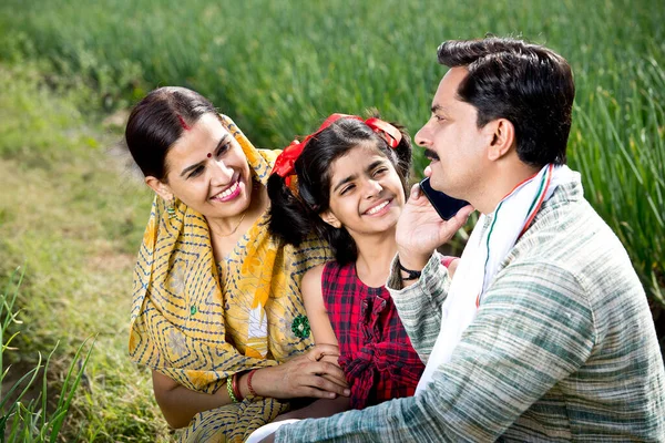 Happy indian family of farmer in agricultural field using phone