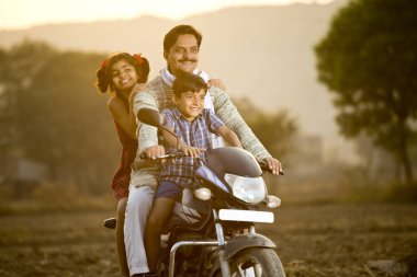 Motosiklet süren çocukları olan mutlu Hintli çiftçi.