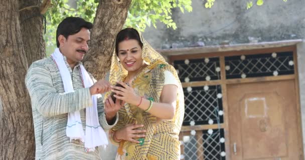 Esposa india rural mirando a su marido mensajes de texto en el teléfono móvil en la aldea — Vídeos de Stock