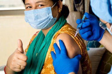 Doktor hastanın koluna aşı enjekte ediyor.