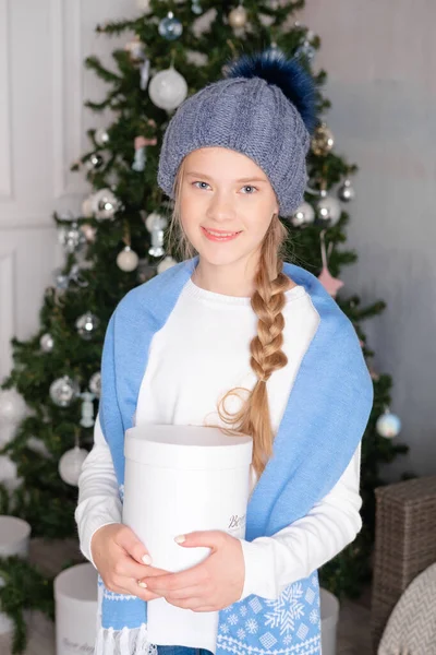 girl opens a gift box. Surprised by the gift. A Christmas gift in the hands of a girl. Surprise for the child. Christmas clothes and interior. Winter hat with pompom