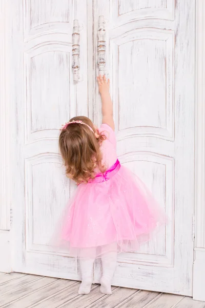 Pembe elbiseli küçük kız. Küçük kız kapıyı açar. Parmak uçlarında bir çocuk. Kız kapı koluna uzandı..