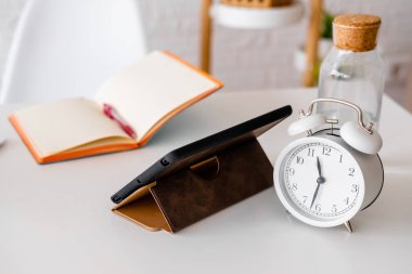 Çalar saat, tablet ve not defteri beyaz bir masada. Ofisteki işyerinde. İş adamı ögeleri