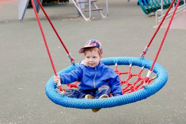 Çocuk salıncakta sallanıyor. Çocuk parkında olağandışı salıncak. Teneffüste eğlence. Çocuklar parkta yürüyor.