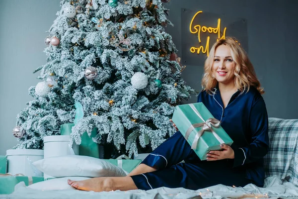 Yataktaki kız hediyeyi açıyor. Sabahleyin pijamalı bir hediyeyi açıyorum. Pijamalı kız şaşkınlıkla gülümsüyor.