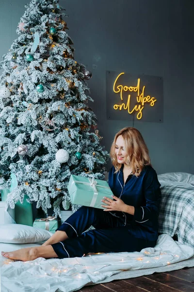 Yataktaki kız hediyeyi açıyor. Sabahleyin pijamalı bir hediyeyi açıyorum. Pijamalı kız şaşkınlıkla gülümsüyor.